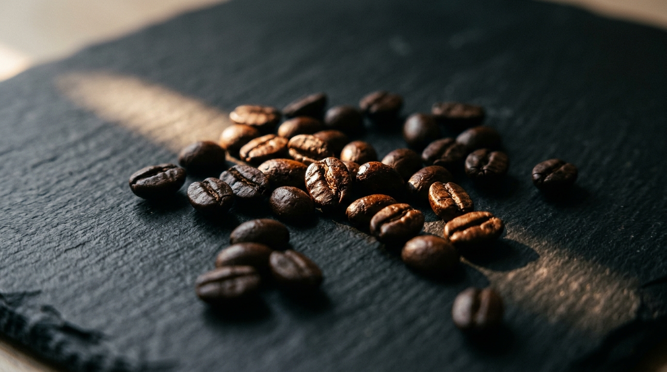 A close-up of a handful of dark roasted espresso beans scattered on a matte blac