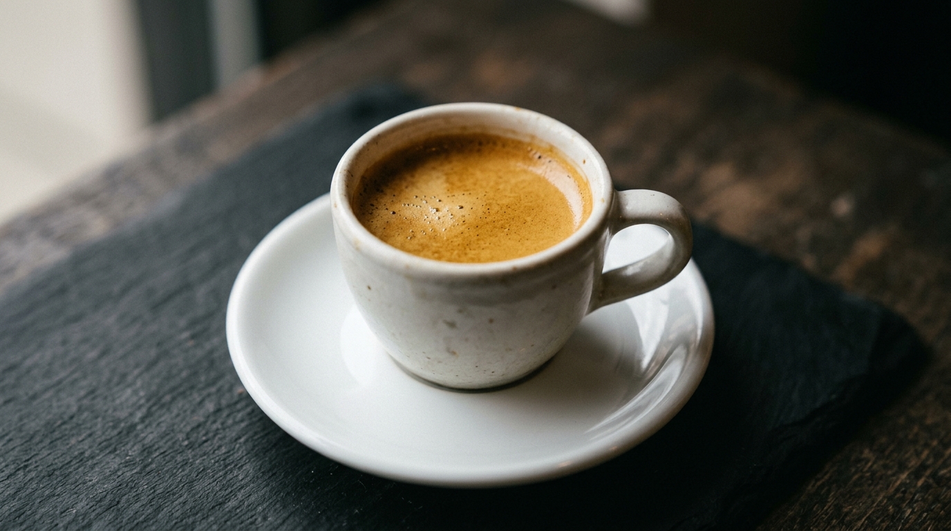 A close-up of a single small ceramic espresso cup resting on a white saucer agai